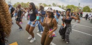 Brightly dressed young women dancing and enjoying an outdoor event on a sunny day.