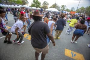 Jumping and dancing at an outdoor community event with diverse participants and tents in the backgro.