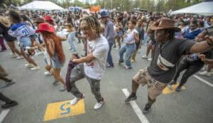 Crowd dancing joyfully at an outdoor event, with diverse participants in casual attire and hats.