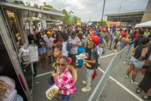 Crowds of people at an outdoor food truck festival with diverse attendees and food stalls.