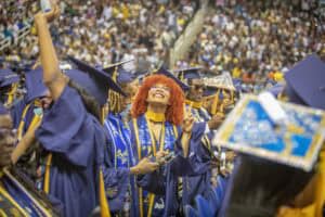 Graduates celebrating at a commencement ceremony in caps and gowns with joyful expressions.