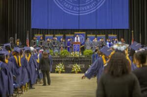 Graduation ceremony at CAES News with students in caps and gowns on stage and audience in attendance.