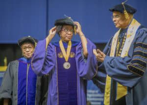 Graduation ceremony with graduates in academic regalia and faculty members on stage.