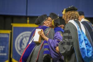 Graduates embrace during a ceremony, celebrating achievements while wearing academic regalia.