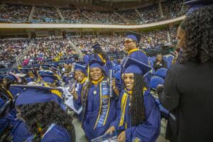 Graduates celebrating at a graduation ceremony in caps and gowns at a large indoor stadium.