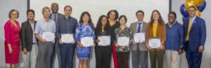 Group of professionals smiling and holding certificates at an awards ceremony, with colorful balloons in the background.