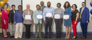 A group of diverse individuals holds certificates in a celebratory setting with balloons in the background.
