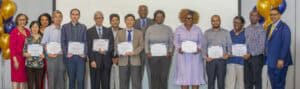 A group of people smiling while holding certificates at a formal event decorated with balloons.