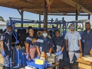 Affordable agricultural workers standing outdoors under a wooden shelter with farming equipment.