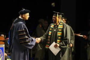 Graduation ceremony with graduate receiving diploma from university official.