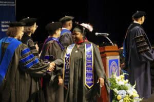 Graduation ceremony with graduates in academic regalia and faculty members on stage.