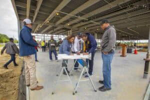 Construction site workers reviewing plans under a large metal roof structure.
