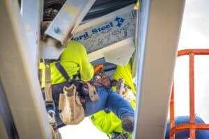 Worker repairing electrical equipment inside a metal enclosure at a construction site.