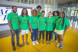 Accessible group of diverse individuals wearing matching green T-shirts at an indoor event, smiling.