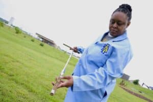 A woman in a blue jacket holding a traditional flute outdoors in a grassy field.