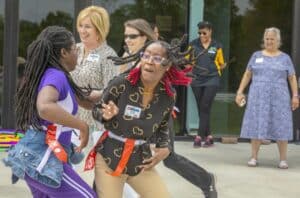 A woman with red braids and glasses dancing outdoors with children and other women at a community ev.