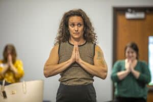 Reflective woman with hands in prayer position during group meditation or prayer session.
