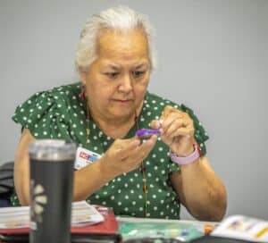 A woman with gray hair and a green polka-dot shirt carefully inspects a small purple object.