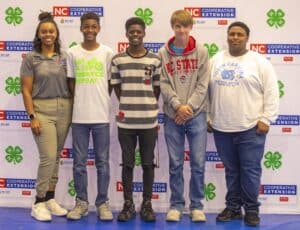 Five young individuals stand side by side, smiling against a backdrop with logos for NC Cooperative Extension and 4-H.