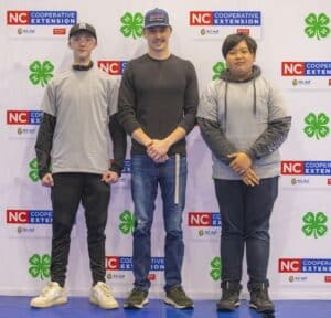 Three individuals stand in front of a NC Cooperative Extension backdrop, smiling and dressed casually.