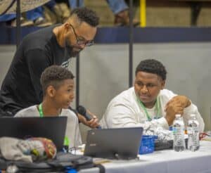 Innovative youth technology workshop with diverse students and mentor at conference table.