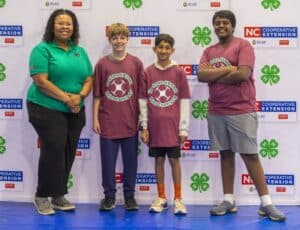 Four people stand together in front of a NC Cooperative Extension backdrop, all smiling and wearing matching t-shirts.