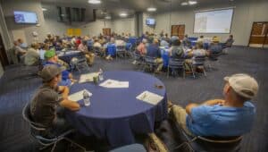 Attendees at a conference or seminar in a large, modern meeting room with presentation screens and r.