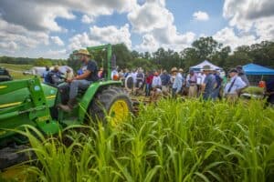 Tractor demonstration at agricultural event with farmers and visitors outdoors.