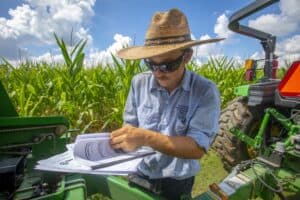 Agricultural researcher inspecting crop data in a cornfield with machinery.