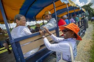 Passengers enjoying a tractor ride at an outdoor event, smiling and interacting under a bright blue sky.