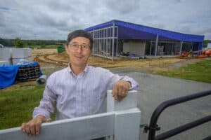 Construction site with a smiling man in front of a partially built blue structure, showcasing ongoin.