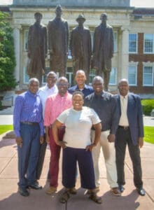 A woman standing in front of a group of men in front of a historic building with statues.