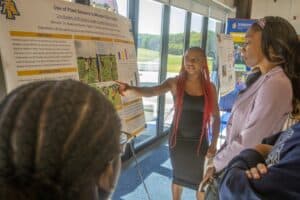 A student presents research on plant health sensors to interested viewers at a presentation event.