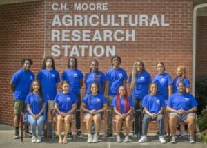 Empowered diverse team of researchers at C.H. Moore Agricultural Research Station in front of brick.
