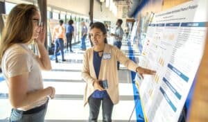 A woman presenting research data on a large poster at a conference.