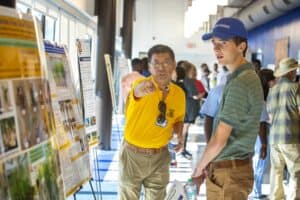 High school science teacher explaining research poster to student at academic conference.