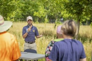Engaging outdoor community meeting with speaker addressing diverse audience in a park setting.