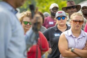 Community gathering with diverse attendees listening attentively at an outdoor event. Focus on engag.