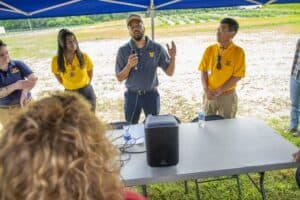 Agricultural expert speaking at outdoor farm event with audience under tent.
