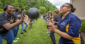 Engaged women participating in outdoor team-building activity with a large black ball.