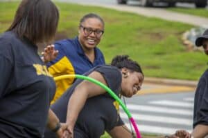 Adults enjoying a playful outdoor activity, smiling and interacting with hula hoops in a grassy area.