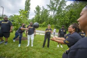 A group of people in NC A&T shirts playing catch with a large black ball outdoors.