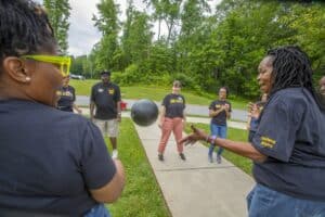 A group of people in matching shirts play with a large ball outdoors, surrounded by trees and greenery.