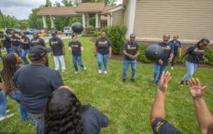 A group of people in matching shirts plays catch with a large ball on a grassy field, enjoying a team-building activity.