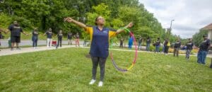 A group engages in a community activity outdoors, with one person using a hula hoop in the foreground.