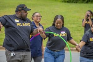 Participants engage in a team-building activity, balancing a hula hoop while holding hands outdoors.