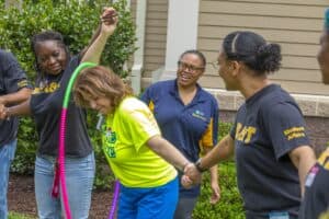 Hispanic woman with a hula hoop, smiling and holding hands with diverse women outdoors.