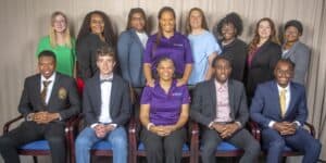 A diverse group of individuals poses together, some seated and others standing, smiling at the camera.