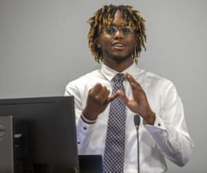 Bright African American man in business attire making a gesture during a presentation at a conferenc.