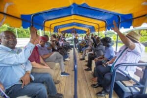 A group of men seated in a colorful vehicle, all raising their hands in response to a speaker.